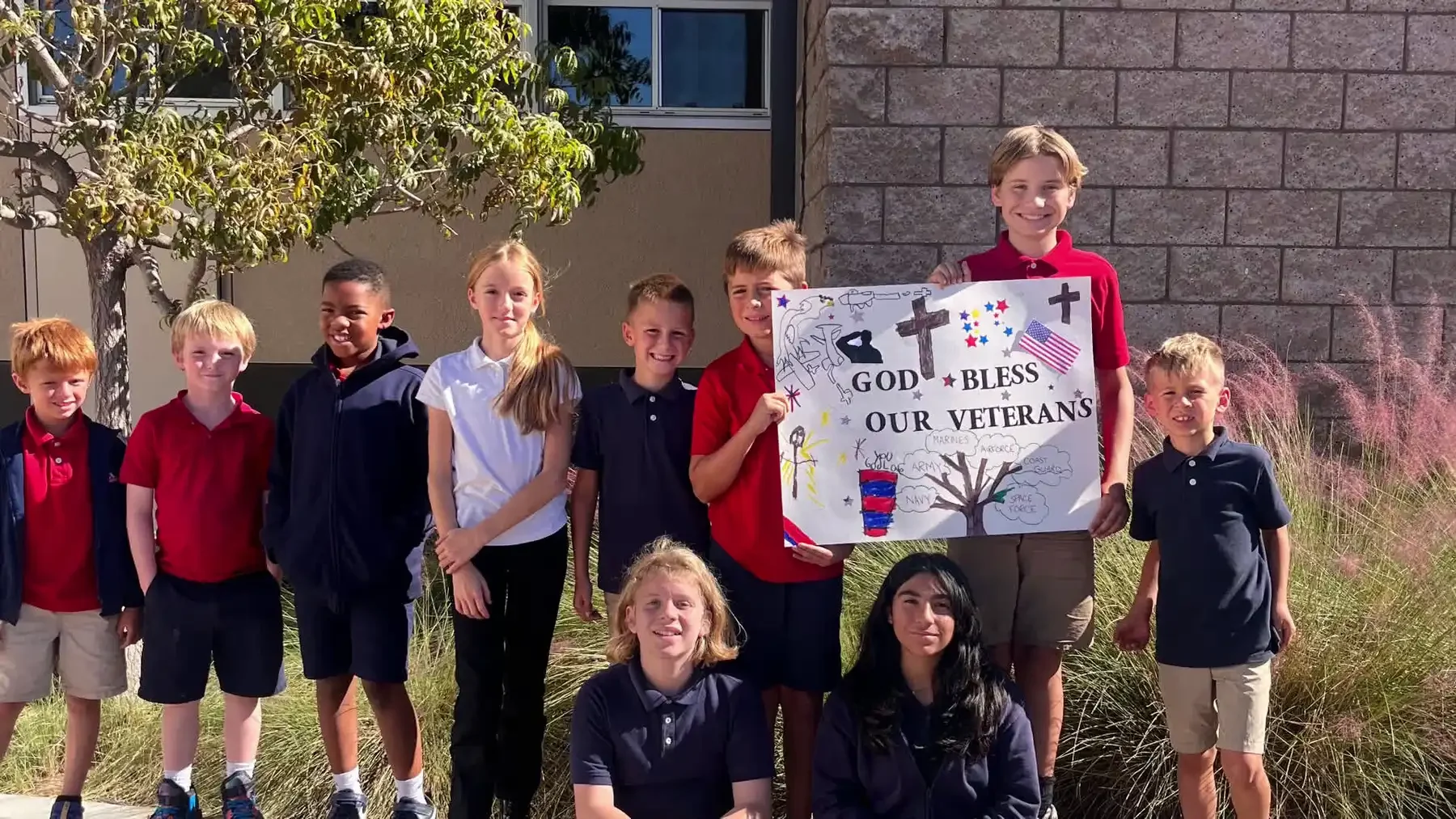 Reformation students outside the school holding a sign reading God Bless Our Veterans