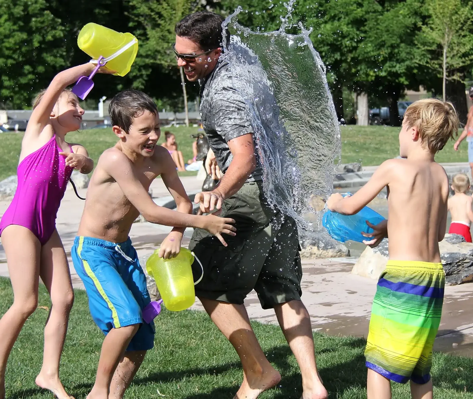 Students and a teacher in a water balloon fight on the grass during summer camp